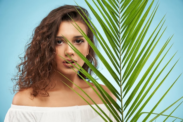 Pretty woman behind palm leaf isolated on blue