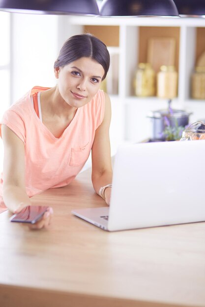 Pretty woman on the phone using laptop at home in the kitchen