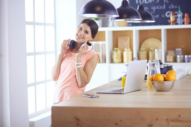 Pretty woman on the phone using laptop at home in the kitchen