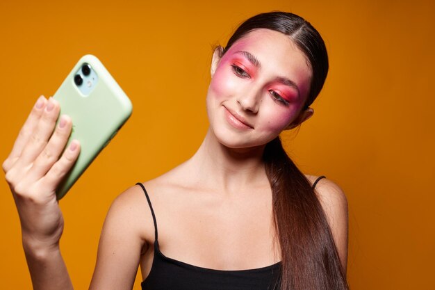 Pretty woman pink face makeup posing attractive look selfie yellow background unaltered