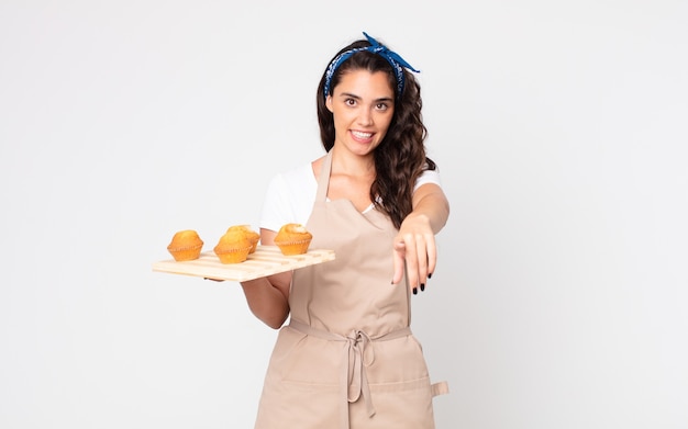 Pretty woman pointing at camera choosing you and holding a muffins tray