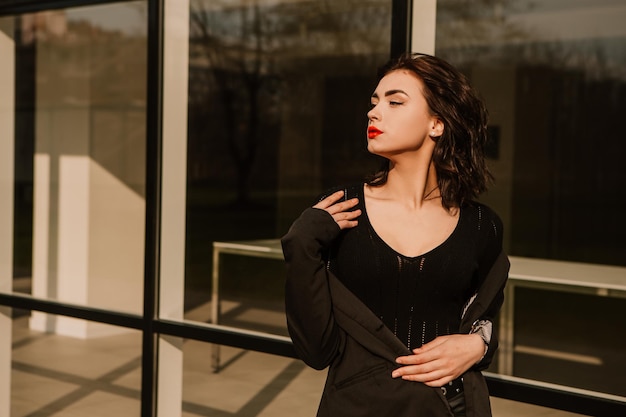 Pretty woman posing near glass building. Girl dressed casual outfits with red lips. Fashion