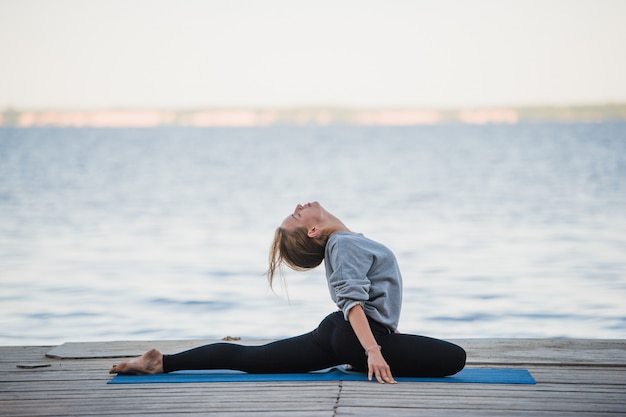 Pretty woman practicing yoga at a lake