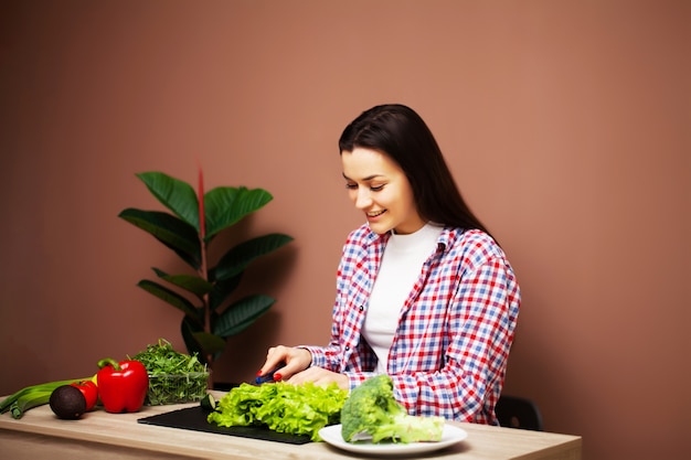 きれいな女性が自宅のキッチンで新鮮な野菜のサラダを準備します。