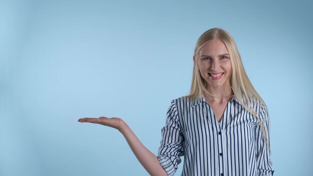 Foto donna graziosa che presenta qualcosa sulla mano vuota con fondo blu