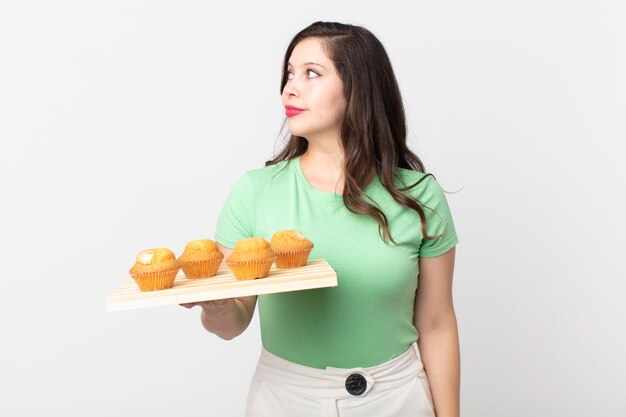 Pretty woman on profile view thinking, imagining or daydreaming and holding a muffins tray