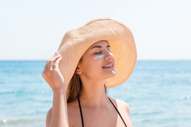 Pretty woman protects her skin on face with sunblock at the beach.