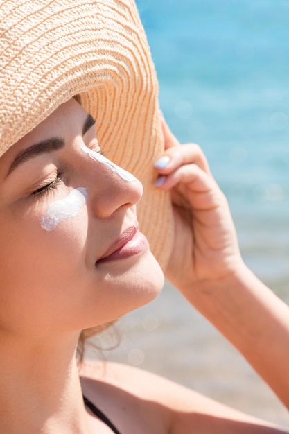 Photo pretty woman protects her skin on face with sunblock at the beach