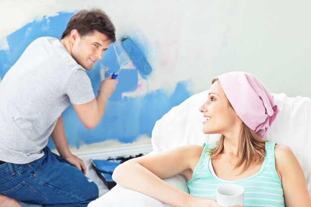 Pretty woman relaxing on a sofa while boyfriend painting the room