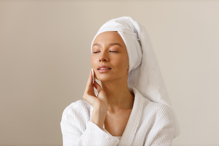 Photo pretty woman in robe and towel on her head wipes the skin of her face with cotton pads cleansing and healthy body care after shower closeup of girl on isolated background