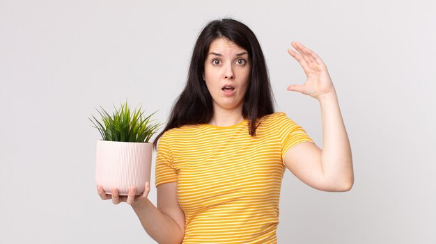 Pretty woman screaming with hands up in the air and holding a decorative plant