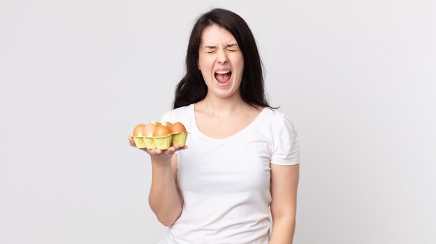 Pretty woman shouting aggressively, looking very angry and holding an eggs box