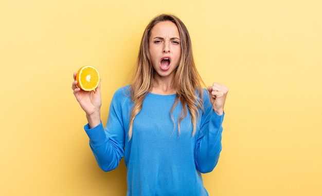 Красивая женщина агрессивно кричит с сердитым выражением лица, держа половину апельсина