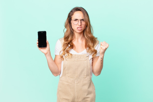 Pretty woman shouting aggressively with an angry expression and holding a smartphone