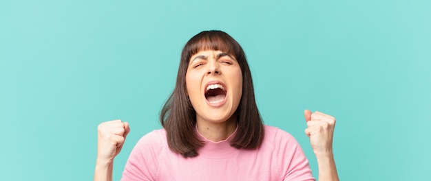 Pretty woman shouting aggressively with an angry expression or with fists clenched celebrating success