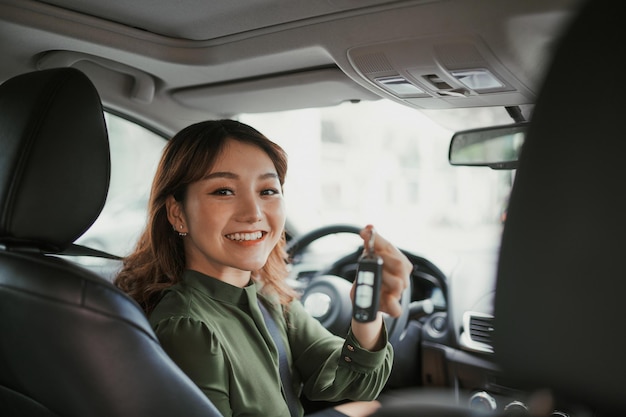 写真 高級車に元気に座って元気に笑っている彼女の新しく購入した自動車で車のキーを示すきれいな女性