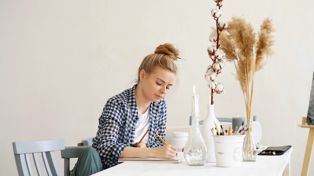 Pretty woman sitting at a table draws in an album with a pencil