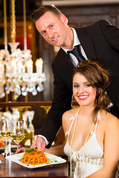 Pretty woman sitting at a table in a fine dining restaurant, waiter served the dinner, a large chandelier is in 