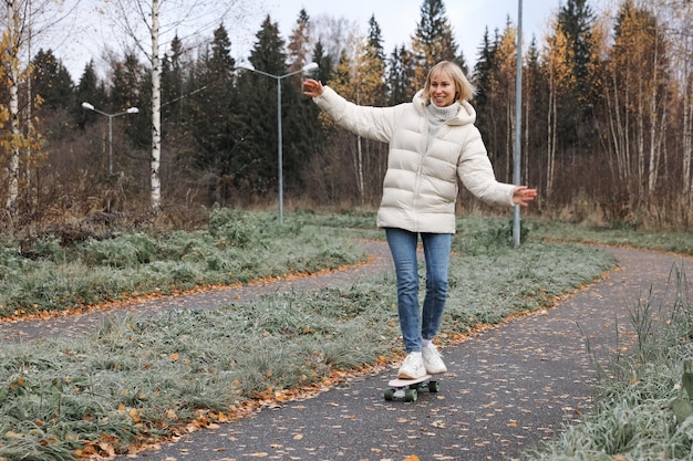 가을 공원에서 스케이트보드를 타는 예쁜 여자, 야외에서 신선한 공기를 마시며 스케이트보드 타는 법을 배우고 있습니다. 건강한 스포츠 개념입니다.