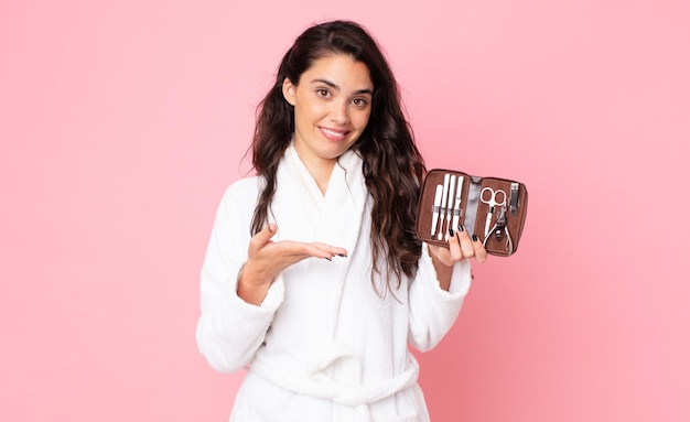 Pretty woman smiling cheerfully, feeling happy and showing a concept and holding a making up bag with nails tools