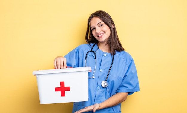 Donna graziosa che sorride allegramente, sentendosi felice e mostrando un concetto. infermiera con con un kit di pronto soccorso infermiera