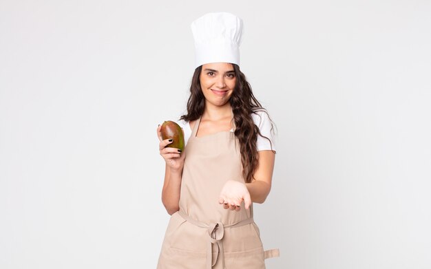 Pretty woman smiling happily with friendly and  offering and showing a concept wearing an apron and holding a mango