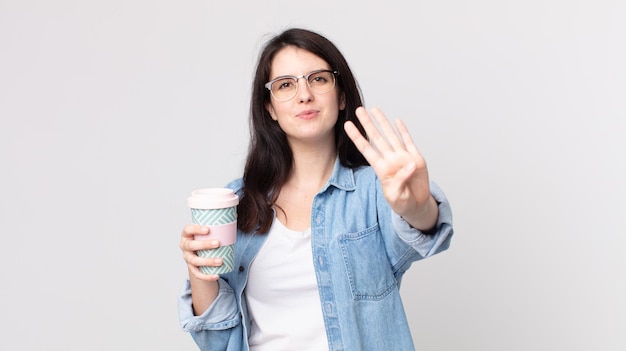 Pretty woman smiling and looking friendly, showing number four and holding a take away coffee