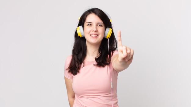 Pretty woman smiling and looking friendly, showing number one listening music with headphones