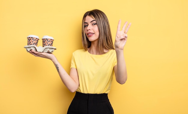 Pretty woman smiling and looking friendly showing number three take away coffees concept