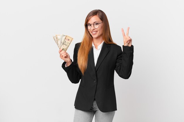 Pretty woman smiling and looking friendly, showing number two. business and dollars concept