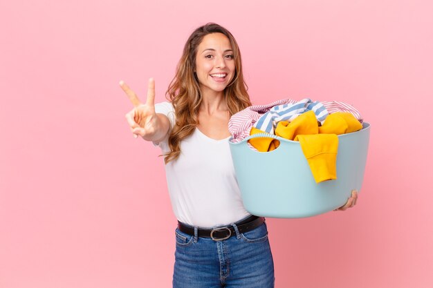 Pretty woman smiling and looking happy, gesturing victory or peace and washing clothes.