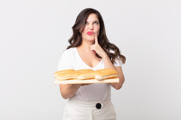 Foto bella donna che pensa, si sente dubbiosa e confusa e tiene in mano un vassoio di pane