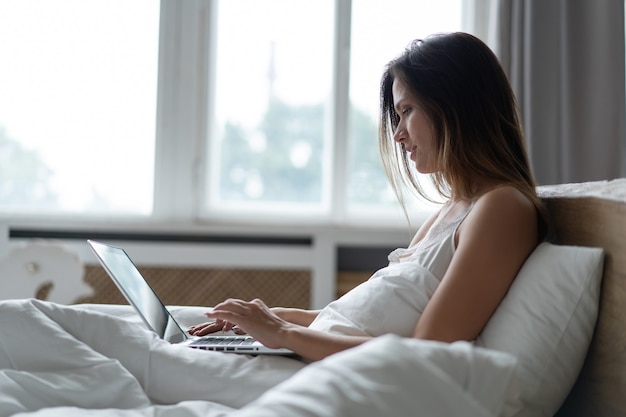 Pretty woman using her laptop in bed.