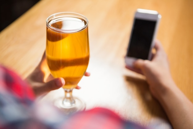 Donna graziosa che per mezzo dello smartphone e mangiando una birra