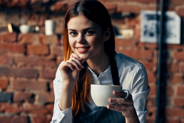 Foto tazza graziosa del cameriere della donna con il muro di mattoni del caffè della bevanda