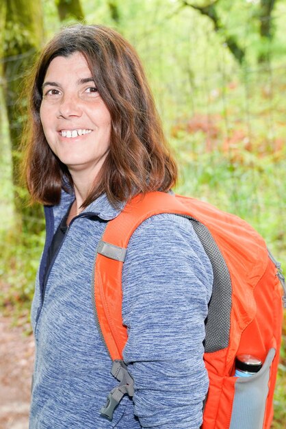 Bella donna che cammina nella foresta in una giornata di sole con lo zaino