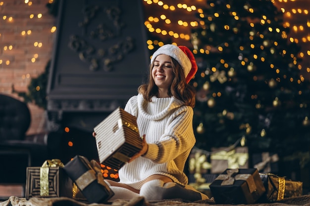 Photo pretty woman in warm sweater, socks and christmas hat, sitting on the floor