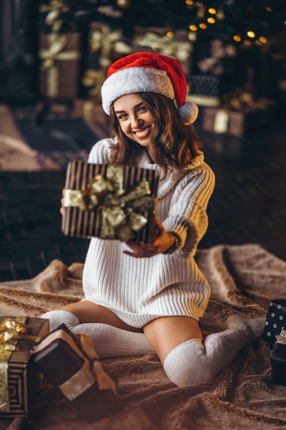 Pretty woman in warm sweater, socks and Christmas hat, sitting on the floor