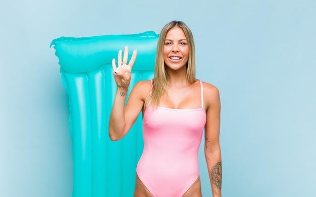 Pretty woman wearing swimsuit smiling and looking friendly, showing number four or fourth with hand forward, counting down