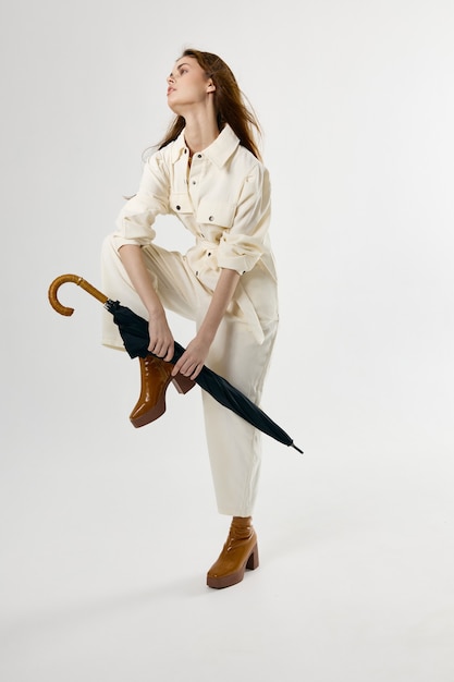 Pretty woman white jumpsuit umbrella in hands bent leg in knee\
studio