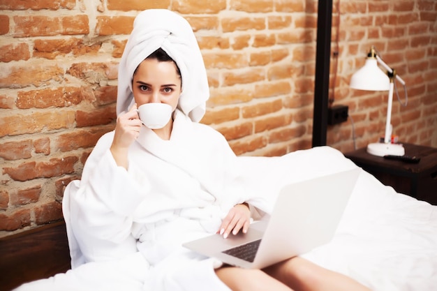 Pretty woman in white towel using her laptop in bed.