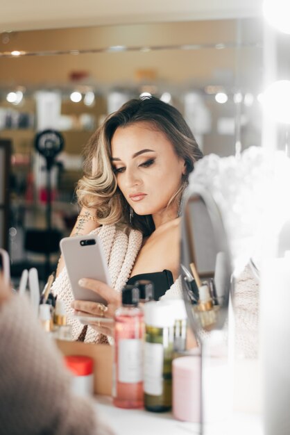 Pretty woman with beautiful makeup takes a selfie in the mirror in the beauty studio