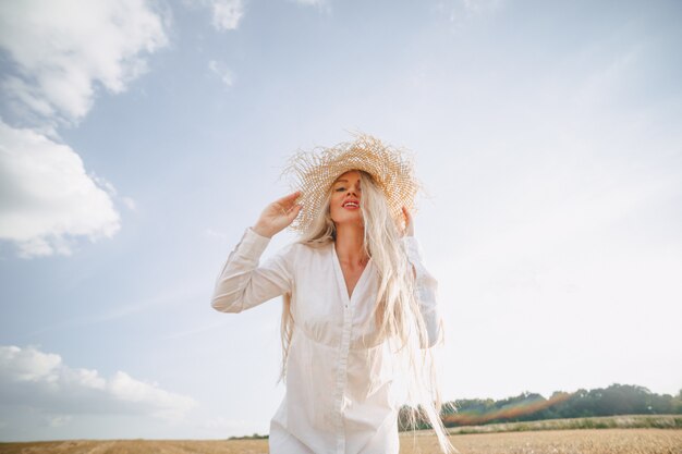 夕暮れ時のフィールドで麦わら帽子のブロンドの長い髪のきれいな女性。夏、農業、自然、そして新鮮な空気。