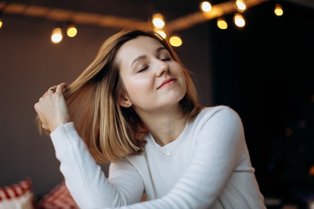 Pretty woman with blonde hair poses in a cosy room decorated for Christmas 