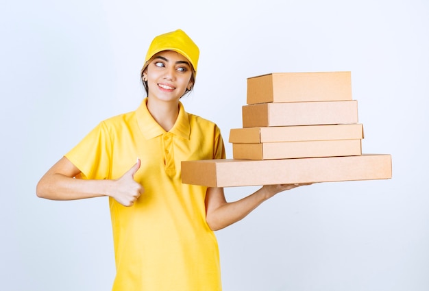 A pretty woman with brown blank craft paper boxes showing a thumb up . 