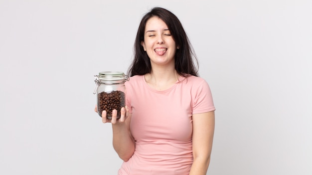 Pretty woman with cheerful and rebellious attitude, joking and sticking tongue out and holding a coffee beans bottle