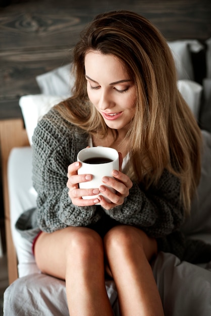 ベッドの上にコーヒーマグカップを持つきれいな女性