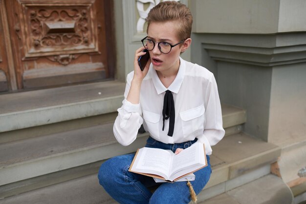 Pretty woman with glasses walking around the city with a book lifestyle high quality photo