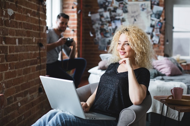 Foto bella donna con un laptop seduto in poltrona e un uomo con una macchina fotografica