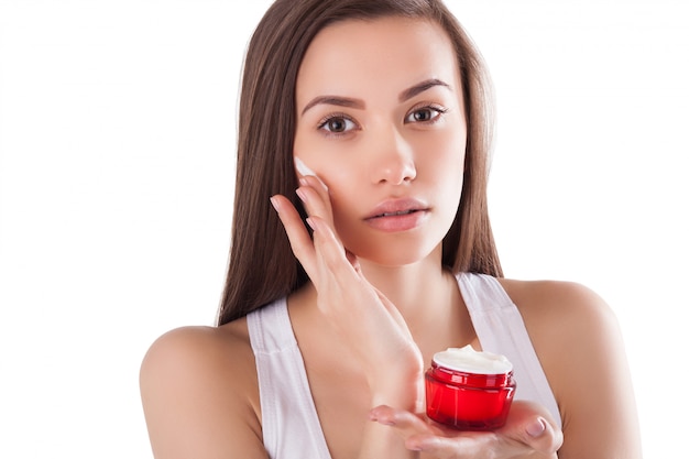 Pretty woman with perfect skin holding a tube with face cream. Young girl with hands on the front. Red jar of cream. Close-up.. Beautiful woman wearing a face and hands cream.